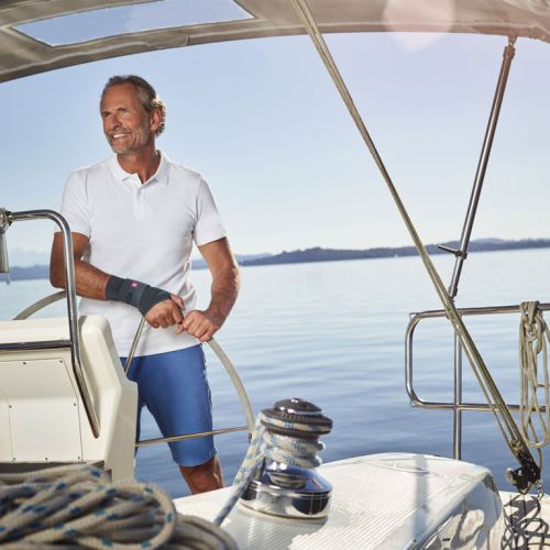 A man on a sailboat wears a wrist brace, showcasing orthopedic support products from medical equipment supplier in Ottawa.